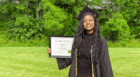 Lassanya Walton proudly holding her JMHS high school diploma while in graduation cap and gown.