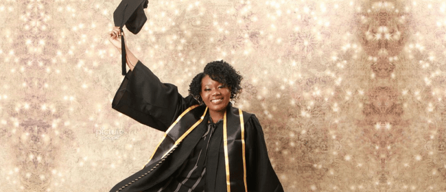 Smiling woman in graduate gown proudly holds up graduation cap against a sparkling background.