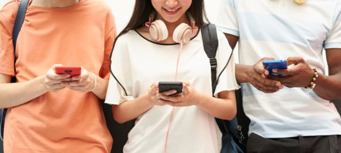 Three high school students, each holding a smart phone in their hands.