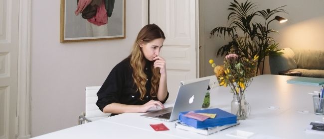 Blonde woman sitting at desk looking at computer.