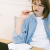 Contemplative young woman biting on pen while sitting in front of an open book and laptop.