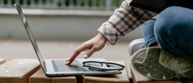 Girl sitting in front of laptop with notebook on lap.