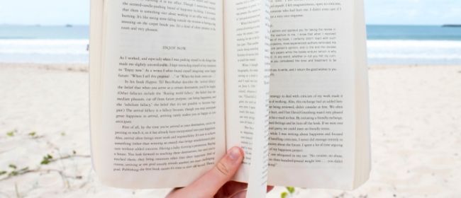 Person holding book at the beach.