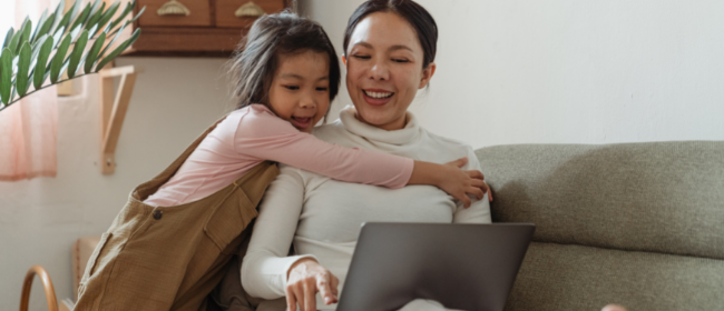 Woman on computer being hugged by daughter.