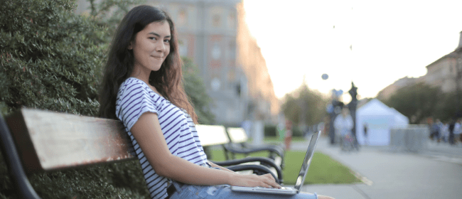 A female teenager sitting on a bench while on her laptop