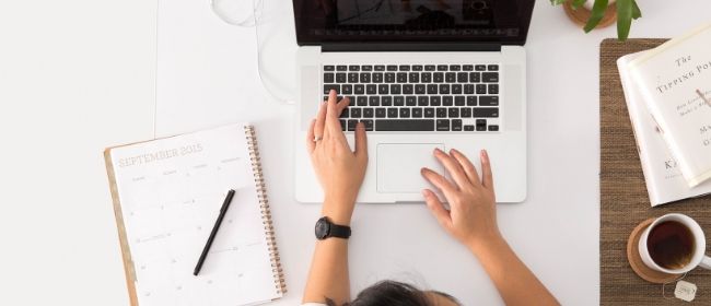 Woman working on laptop with notebook.