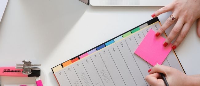 Woman writing on pink post-it note.