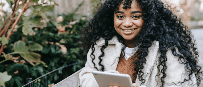 Smiling teenage girl holding a tablet while outside.