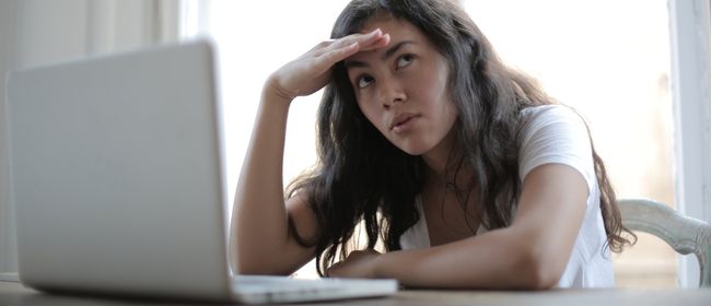 Teenage girl sitting in thought while in front of an open laptop computer.