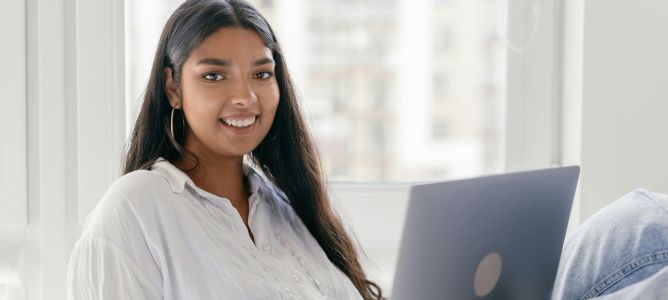 Girl with brown hair in white shirt holding laptop.