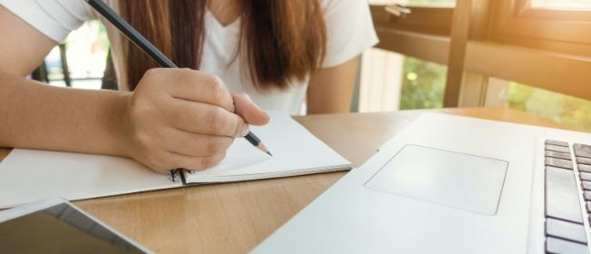 Girl taking notes by laptop.