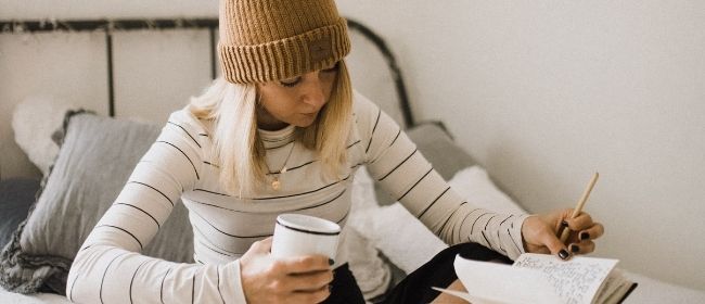 Girl sitting on bed holding cup and looking at notebook